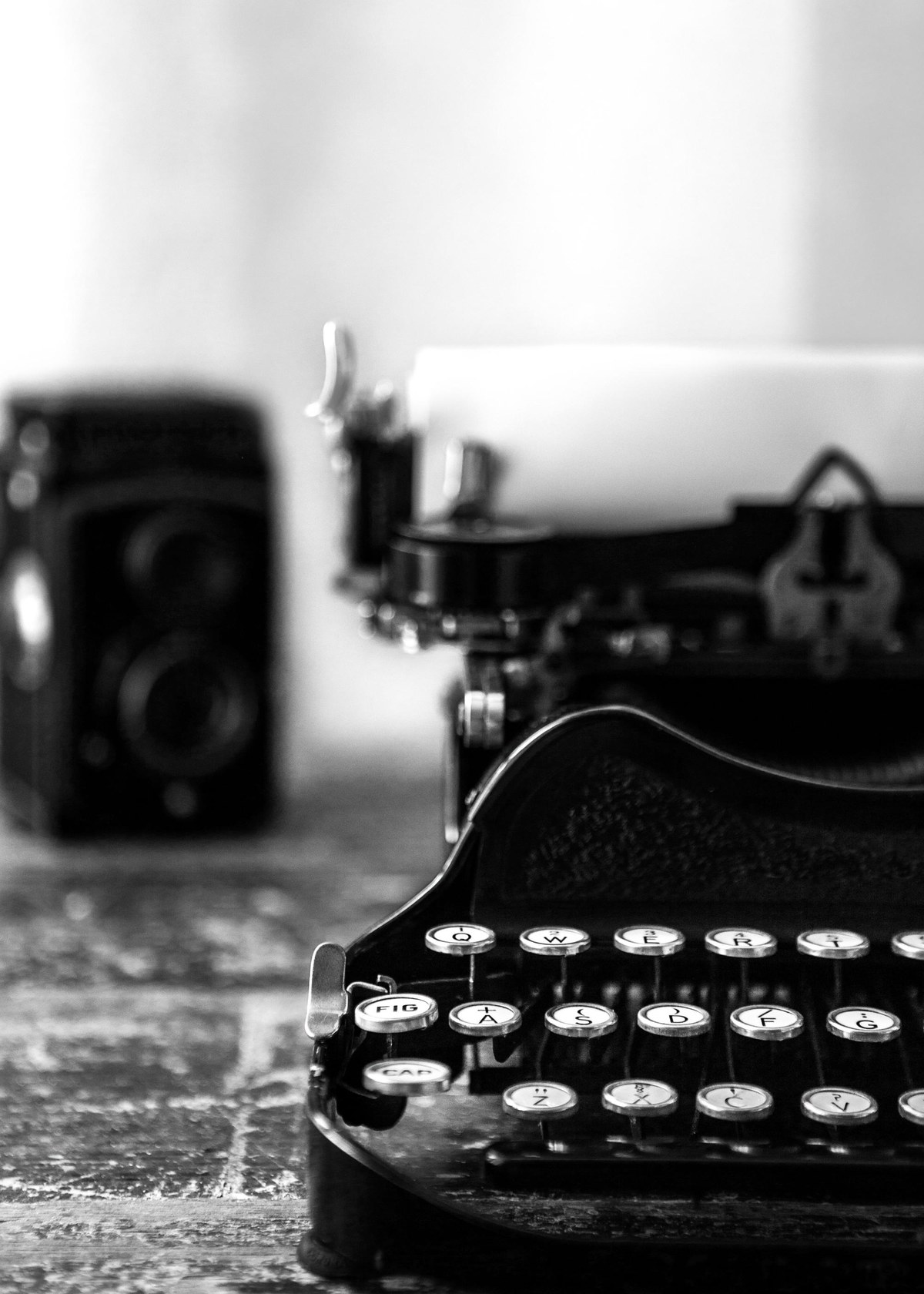 A vintage manual typewriter and twin-lens camera on a weathered wooden desk.